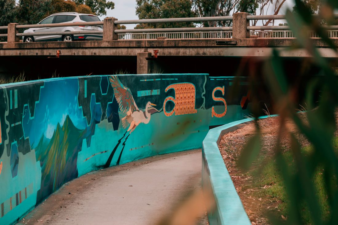 A mural featuring a bird and abstract shapes, running under a road underpass.